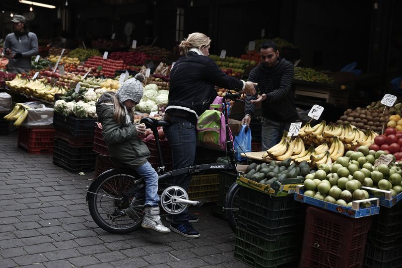 A woman pays for vegetables as her child sits on a bicycle at a market in central Athens, on Monday, Feb. 9, 2015. Investors hammered Greece's markets on Monday after the country's new government renewed a pledge to seek bailout debt forgiveness, setting up a clash with European lenders. (Petros Giannakouris / Associated Press)