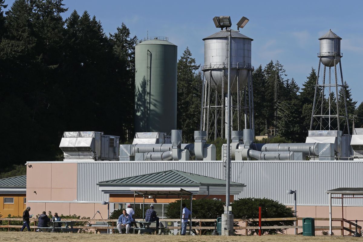 In this Sept. 15, 2017, photo, residents sit in a yard at the Special Commitment Center on McNeil Island, Wash., with the current water tower that serves the facility behind them at left, next to two older and currently unused towers. (Ted S. Warren / Associated Press)