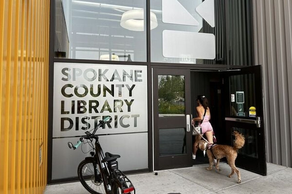 A woman and her dog walk through the doors at the Spokane Valley Library, one of 10 libraries in the Spokane County Library District. (Emily White / The Spokesman-Review)
