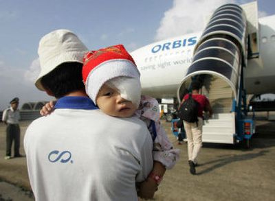 
A man carries his son toward New York-based ORBIS International's flying eye hospital, a converted DC-10 complete with operating room, at the airport in Danang, Vietnam, on Friday. 
 (Associated Press / The Spokesman-Review)