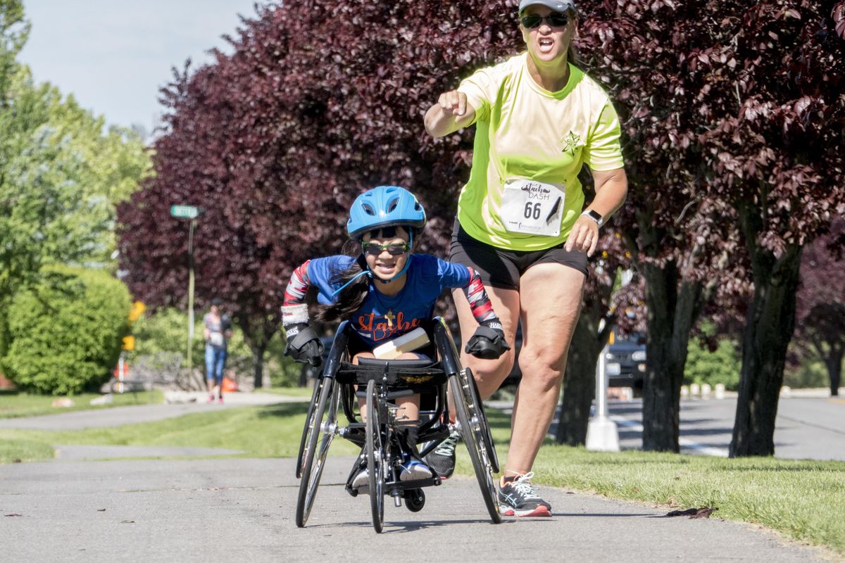 Ruby Floch, 12, speeds away on her wheelchair Saturday after Stacy Franklin, right, gave her quick push while competing in the Stache Dash  at Pavilion Park in Liberty Lake. Franklin is a pediatric physical therapist who works with Floch and accompanied her on the 5-K run. (Jesse Tinsley / The Spokesman-Review)