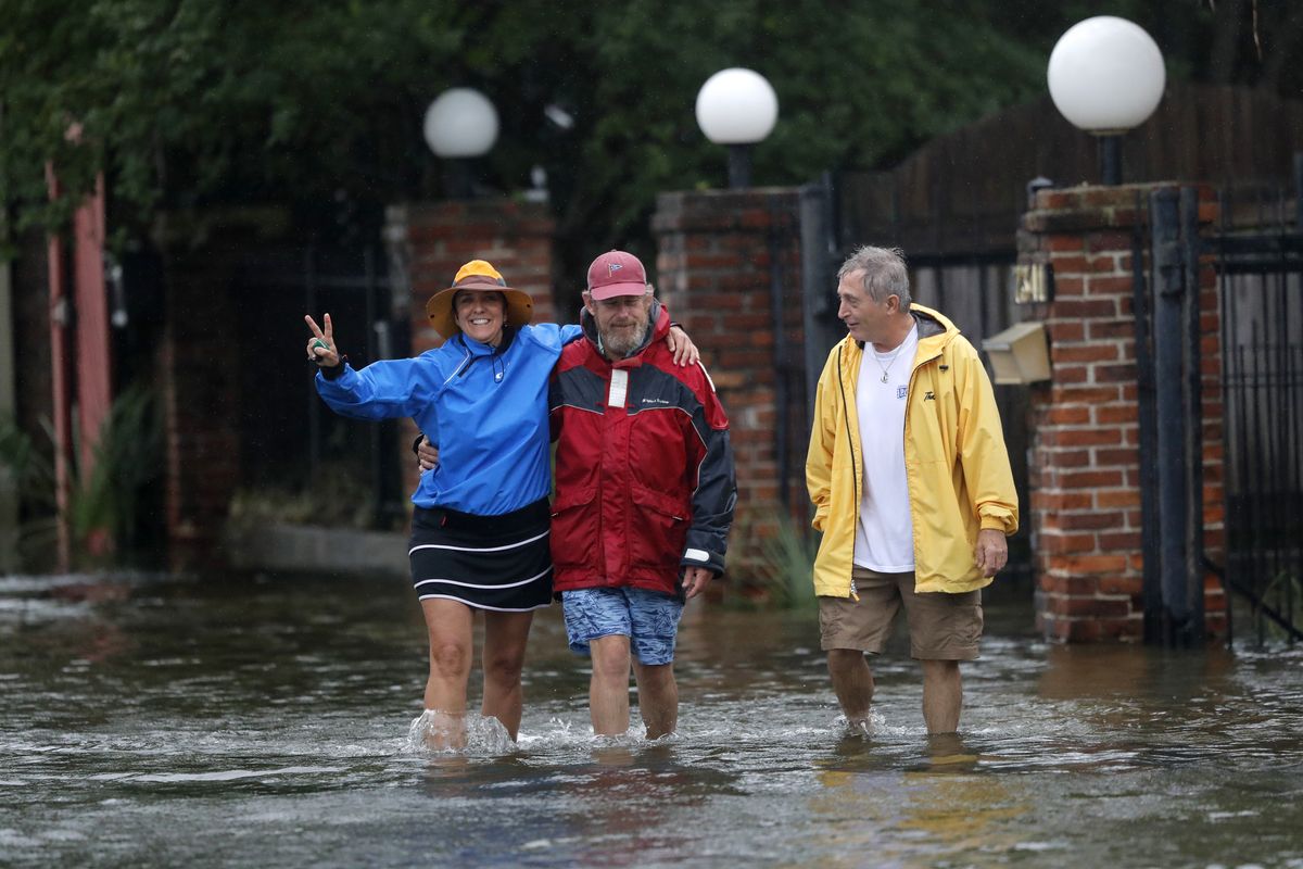 Isabelle Schneidau, left, gestures to the camera as she walks in a rising storm surge with Mont Echols, center, and L.G. Sullivan, right, after checking on their boats in the West End section of New Orleans in advance of Tropical Storm Cristobal in New Orleans, Sunday, June 7, 2020.  (Gerald Herbert)