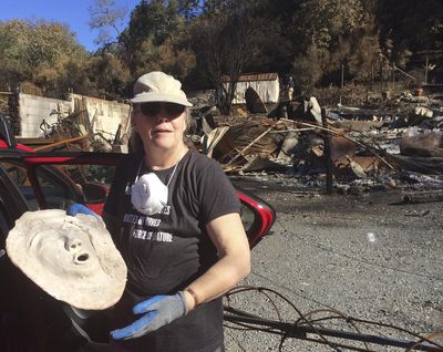 Joyce Farinato, a pastor and artist who lost her Glen Ellen, Calif., home in recent wildfires, stands in the ruins Monday, Oct. 23, 2017, and shows a mask she found in the debris, one of her few surviving possessions. (Ellen Knickmeyer / Associated Press)