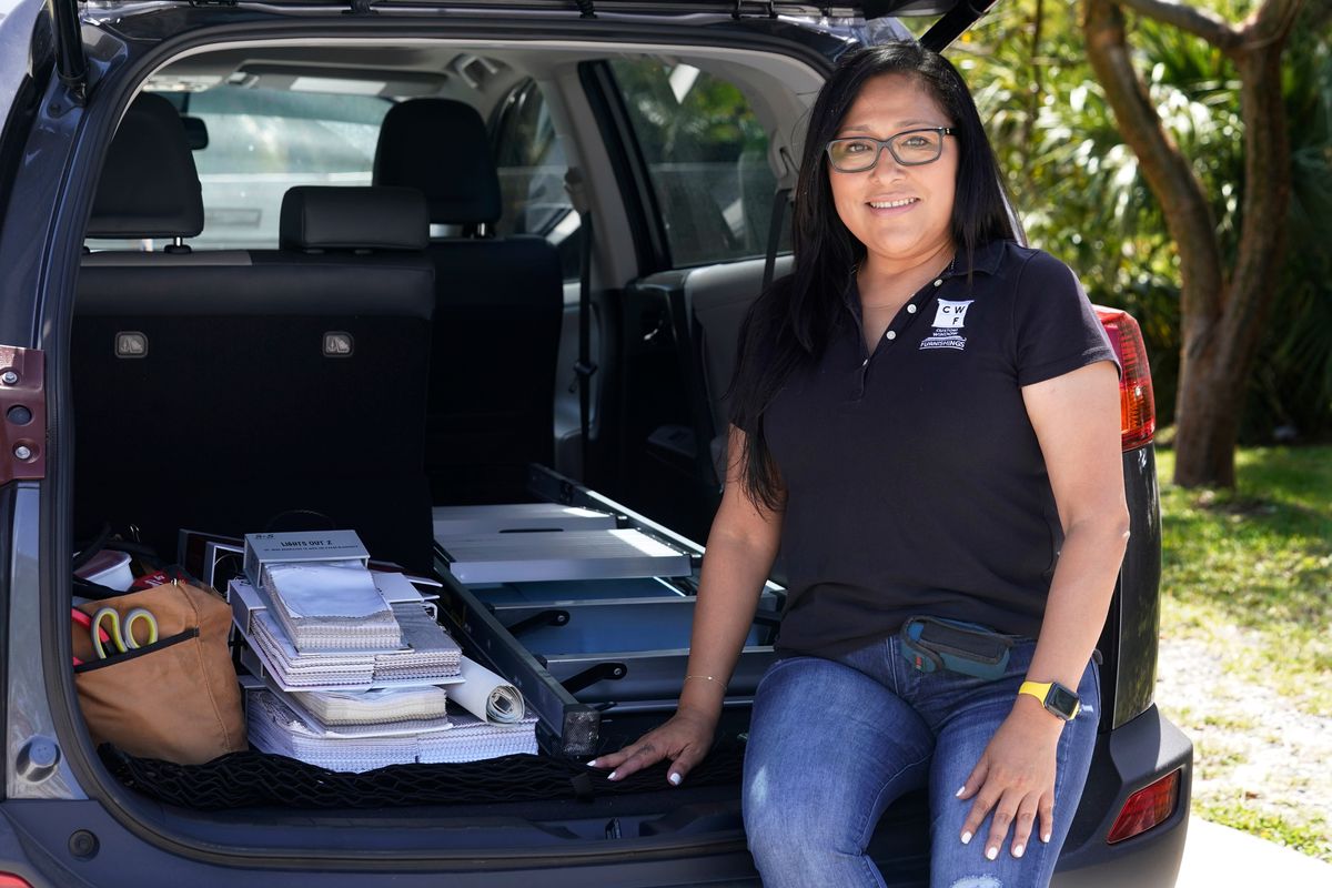 Natalia Ponce De Leon, owner of Custom Window Furnishings, sits on the back of her nine-year-old Toyota RAV4 after visiting with a client, Wednesday, April 13, 2022, in Delray Beach, Fla. Ponce De Leon traded her 2018 Toyota Tacoma for a more efficient car where she estimates will save her hundreds of dollars a month. She is also able to carry all the tools she needs for her business.  (Marta Lavandier)