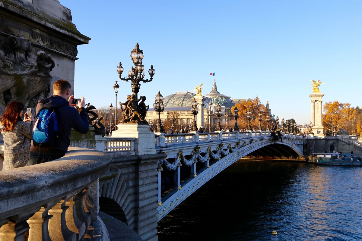 Tourists take pictures on the Alexandre III bridge with the Grand Palais in the background last November. (Paris Convention and Visitors Bureau)