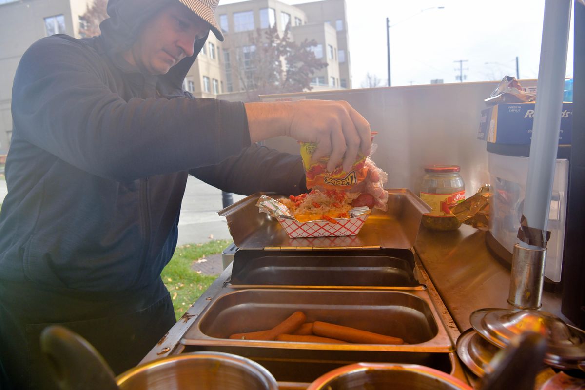 Seam shrouds James Quinn, owner of Steam Dog Express as he assembles his Beefy Cheesy Spicy Crunchy Monster Dog on Thursday, Oct. 31, 2019, at the Spokane County Courthouse in Spokane, Wash. The BCSC Monster dog features a beef sausage, nacho cheese and is topped with flaming hot Cheetos. (Tyler Tjomsland / The Spokesman-Review)