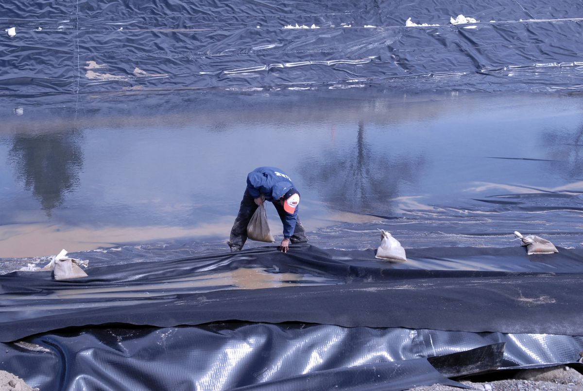 Julio Juarez of Wadsworth Golf Construction Co. places sandbags on fabric over heavy duty plastic sheets for pond rocks at one of the new water features at Liberty Lake. (J. Bart Rayniak / The Spokesman-Review)