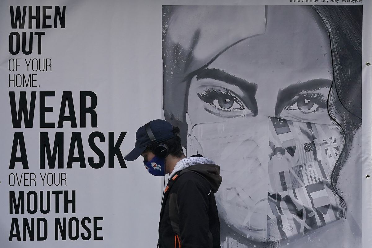 FILE - In this Nov. 21, 2020, file photo, a pedestrian walks past a mural reading: "When out of your home, Wear a mask over your mouth and nose," during the coronavirus outbreak in San Francisco. From speculation that the coronavirus was created in a lab to a number of hoax cures, an overwhelming amount of false information about COVID-19 has followed the virus as it circled the globe over the past year.  (Jeff Chiu)