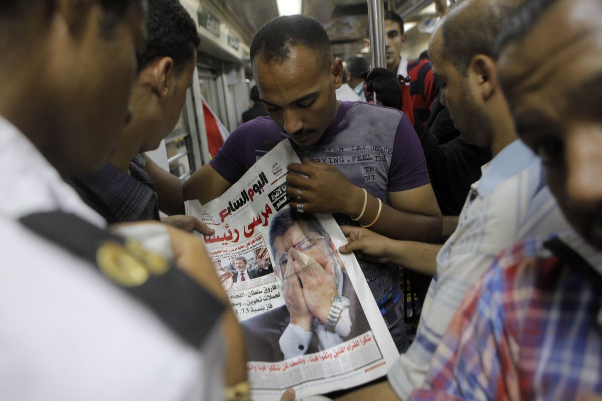 Egyptians in Cairo read a newspaper Monday fronted by a picture of Egypt’s newly elected President Mohammed Morsi. (Associated Press)