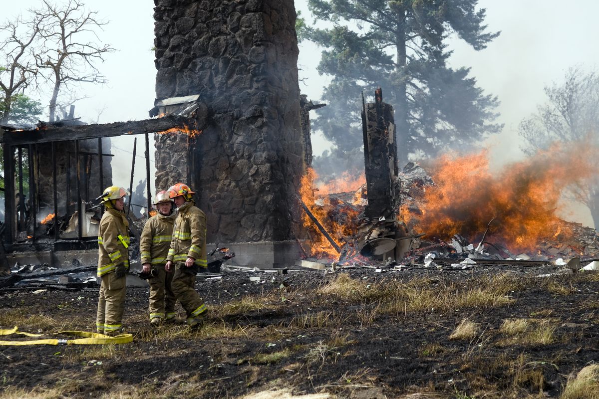 Spokane County firefighters stand next to a house at 16102 S. Wood Road that was destroyed when a tree hit a power line, which created a surge into the home. The fire also burned several acres of hayfield, but was quickly contained despite the high winds. No injuries were reported.  (Colin Mulvany)