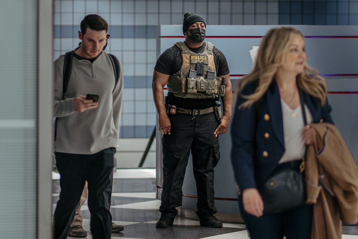A masked Immigration and Customs Enforcement agent stands near an exit at Terminal 1 at O