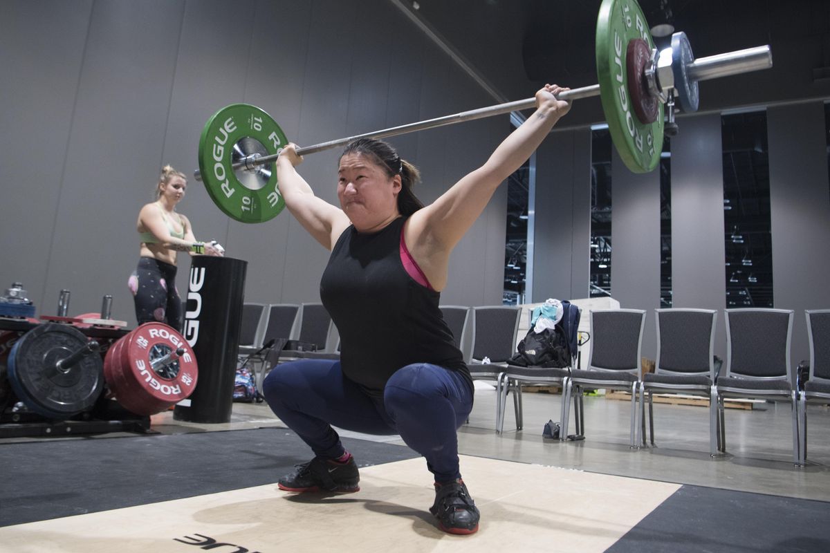 April Roach snatches a bar over her head and settles into a squat while working out Thursday, Feb. 15, 2018 at the Spokane Convention Center  in preparation for the weightlifting event Friday and Saturday. While Roach is an avid competitor, she’ll actually be officiating at the Junior Nationals and the Washington State Championships this weekend. In the background is Alexis Danchak, another lifter who will be officiating. (Jesse Tinsley / The Spokesman-Review)