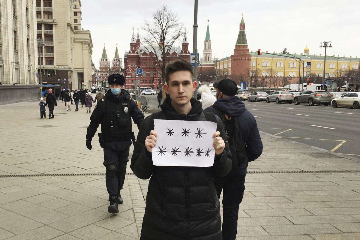 Police officers, left, prepare to detain Dmitry Reznikov holding a blank piece of paper with eight asterisks that could have been interpreted as standing for "No to war" in Russian, with the Kremlin in the background in Moscow, Russia, on Sunday, March 13, 2022. A court found him guilty of discrediting the armed forces and fined him 50,000 rubles ($618) for holding the sign in a demonstration that lasted only seconds before police seized him.  (HONS)