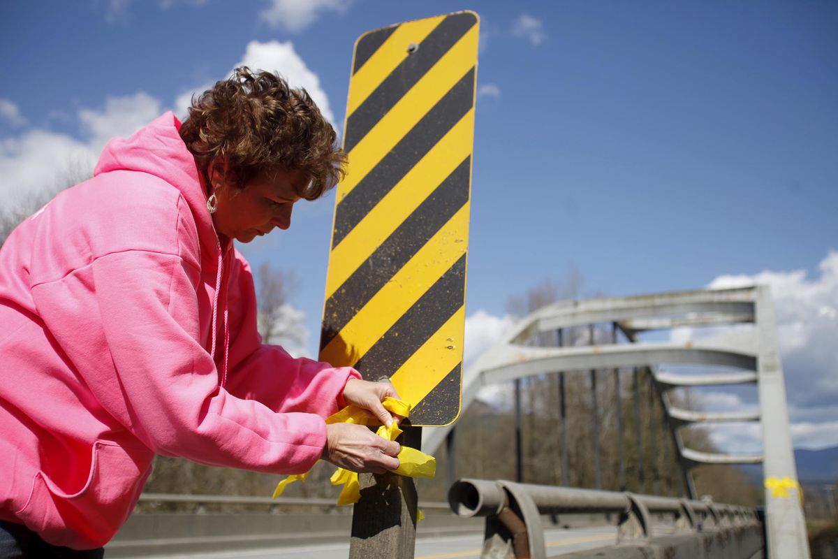 Debra Hoskins ties yellow bows on a bridge on highway 530, Tuesday, April 1, 2014, in near Arlington, Wash. Hoskins said, "The bows signify to hold onto your faith and keep believing." (Sofia Jaramillo / The Herald)