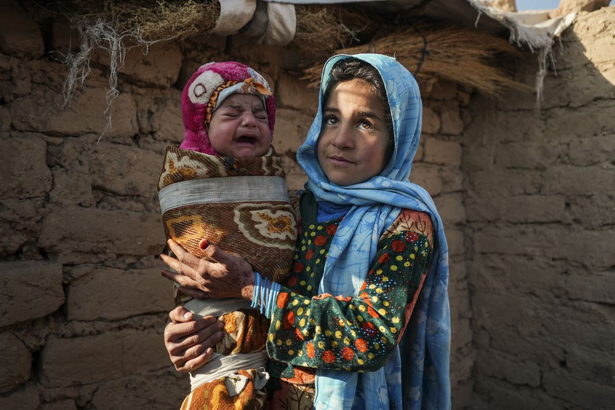 Qandi Gul holds her brother outside their home housing those displaced by war and drought near Herat, Afghanistan. Dec. 16, 2021. Gul’s father sold her into marriage without telling his wife, taking a down-payment so he could feed his family of five children. Without that money, he told her, they would all starve. He had to sacrifice one to save the rest.  (Mstyslav Chernov)