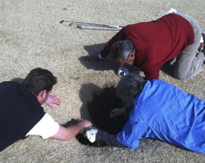 Hank Martinez, top, Ed Magaletta, right, and Russ Nobbe, look into an 18-foot-deep sinkhole that golfer Mark Minhal fell into in Missouri. (Associated Press)