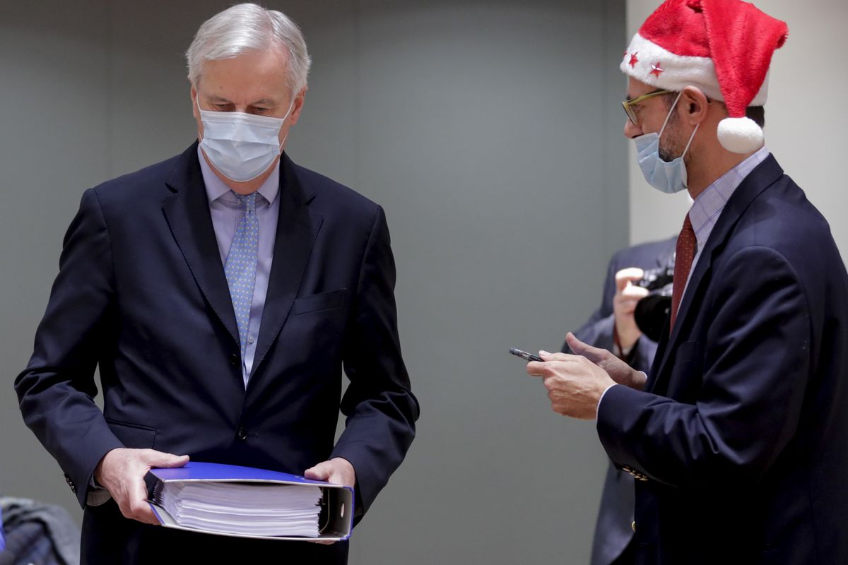 A collegue wears a Christmas hat as European Union chief negotiator Michel Barnier, left, carries a binder of the Brexit trade deal during a special meeting of Coreper, at the European Council building in Brussels, Friday, Dec. 25, 2020. European Union ambassadors convened on Christmas Day to start an assessment of the massive free-trade deal the EU struck with Britain. After the deal was announced on Thursday, EU nations already showed support for the outcome and it was expected that they would unanimously back the agreement, a prerequisite for its legal approval.  (Olivier Hoslet/Associated Press)