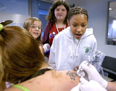 From left, Felicia Pollos, 9, Kayli Behrens, 11, and Lexi Montgomery, 10, watch as Anita Behrens has her tattoo filled in by tattoo artist Dan Golebiewski at the Protect the Innocent benefit Saturday in Post Falls.  
 (Joe Barrentine / The Spokesman-Review)