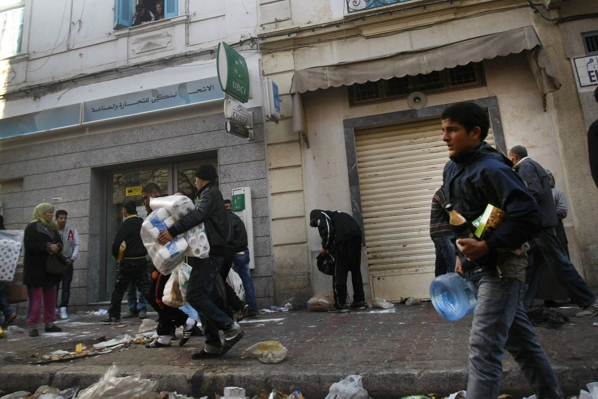 In this photo taken through a window, people are seen looting  goods from a  store in Tunis, Tunisia, Saturday.  (Associated Press)