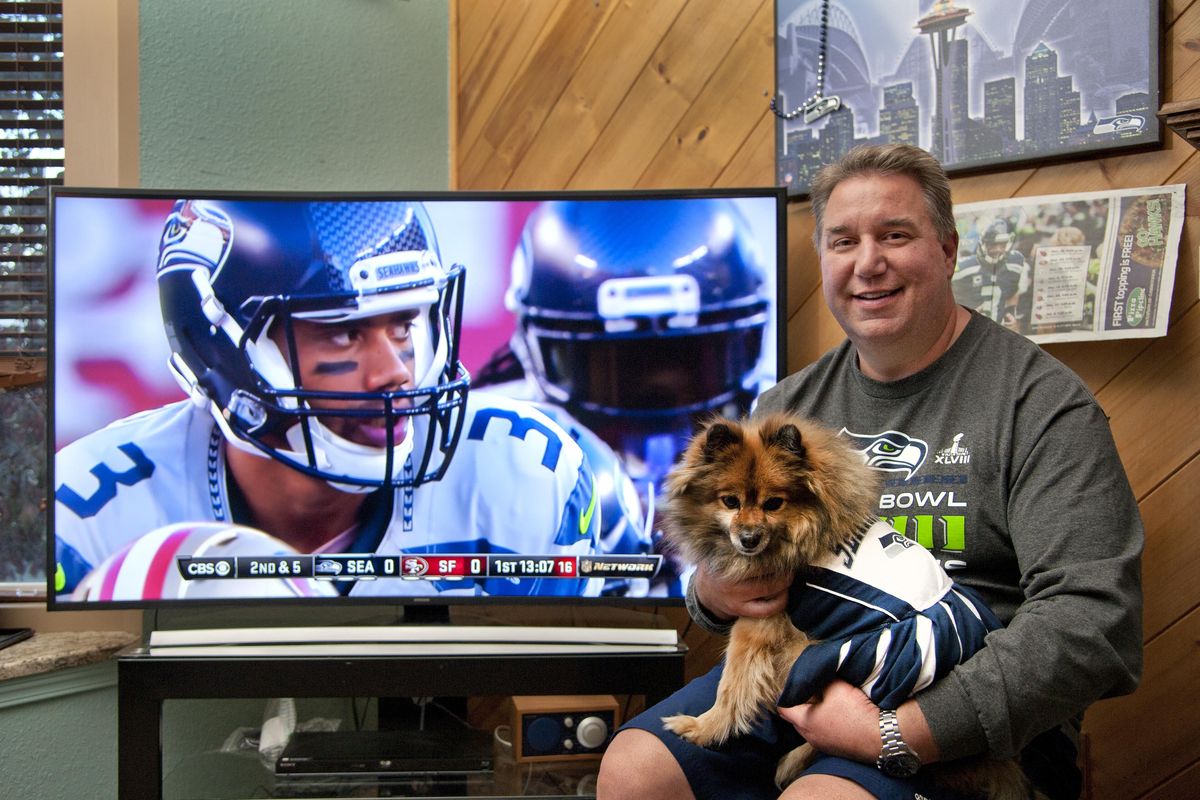 A Seattle merchandise store has partnered with the animal rights organization PAWS to hold a "12th Dog" online fundraiser. Spokane resident Gerry Bozarth has entered his Pomeranian, Lacy, in the competition. Here they watch the Seahawks play the 49ers on TV, Oct. 22, 2015. DAN PELLE danp@spokesman.com (Dan Pelle / The Spokesman-Review)