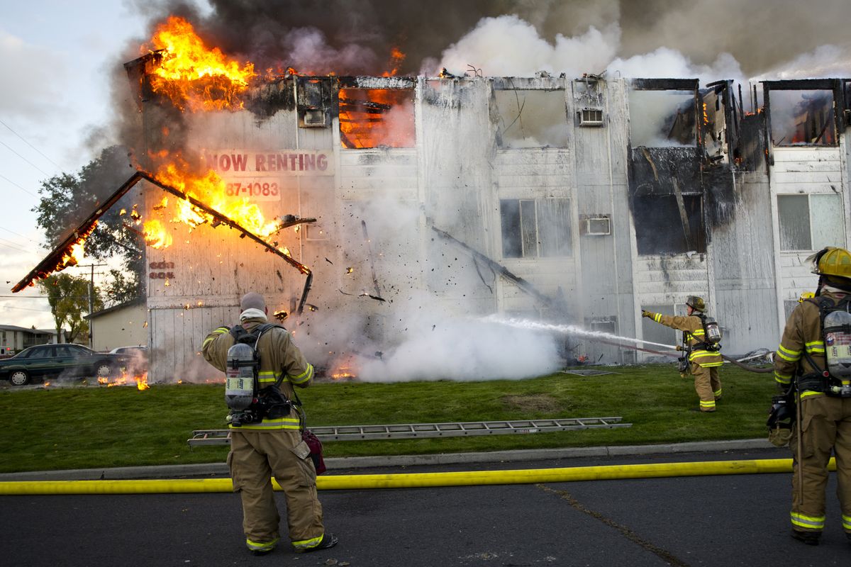 A burning roof eave falls away as Spokane Fire Department firefighters battle a fire at the Houston Apartments at 607 E. Houston Ave. Eighty-five residents in 29 units were safely evacuated during the three-alarm fire Sunday afternoon.  (Colin Mulvany)