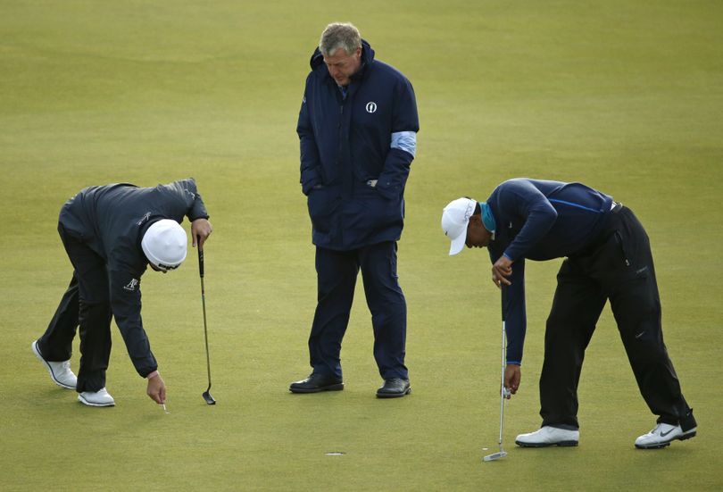 United States’ Tiger Woods, right, and South Africa’s Louis Oosthuizen, left, mark their balls on the 13th green as an official stops play due to strong winds during the second round of the British Open at the Old Course, St. Andrews, Scotland on Saturday. (AP)