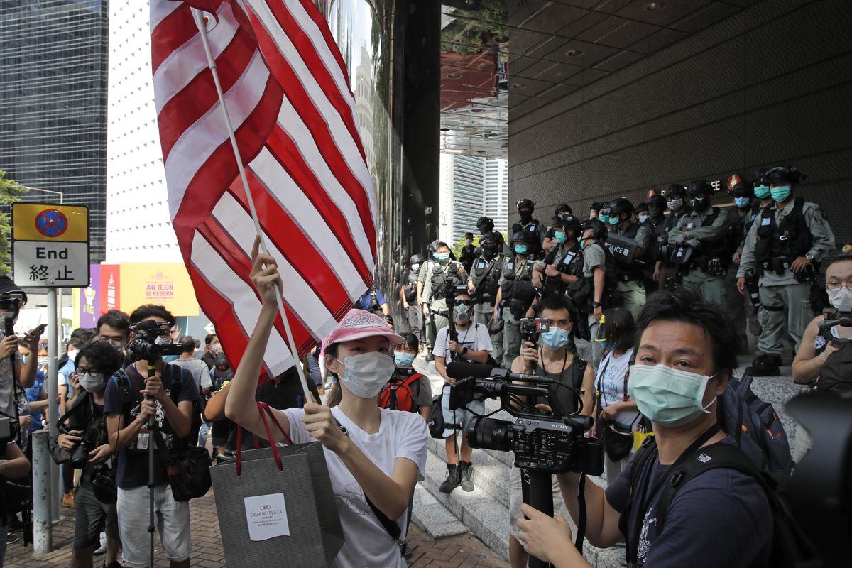FILE - In this July 4, 2020, file photo, a woman carries an American flag during a protest outside the U.S. Consulate in Hong Kong. The U.S. has issued a new advisory Tuesday, Sept. 15, 2020, warning against travel to mainland China and Hong Kong, citing the risk of "arbitrary detention" and "arbitrary enforcement of local laws." (Kin Cheung)