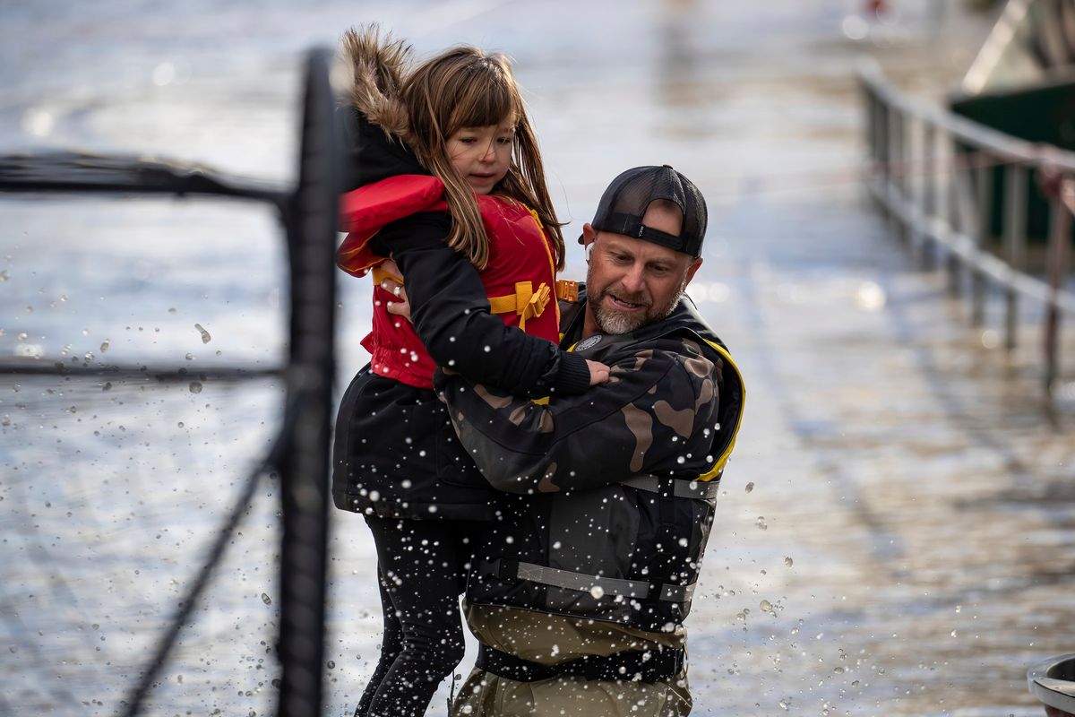 A volunteer carries a young girl to high ground Tuesday after using a boat to rescue a woman and children who were stranded by high water due to flooding in Abbotsford, British Columbia. Officials in Sumas, Wash., said Tuesday that hundreds of people had been evacuated and estimated 75% of homes had water damage.  (Darryl Dyck)