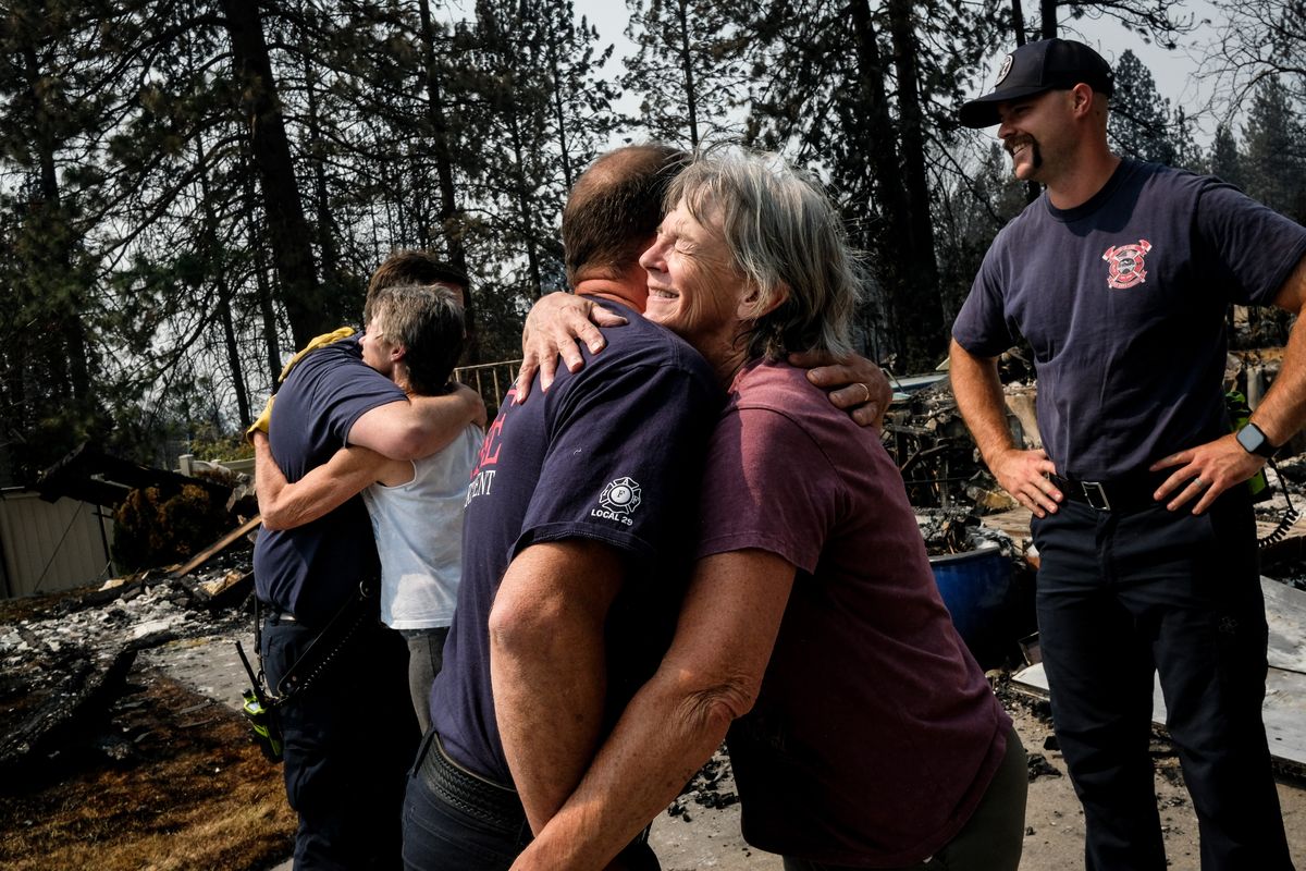 Spokane Fire Lt. Brandon Bacon, left, hugs homeowner Suzanne Johnson and fire equipment operator Jerry Sander embraces Johnson’s sister, Bridget Reilly, on Sunday in northwest Spokane. Firefighter Noah Plowman looks on as the group visits the area scorched by the Old Trails fire. (Tyler Tjomsland/The Spokesman-Review)