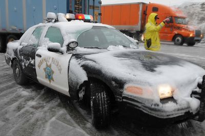 A California Highway Patrol officer turns traffic around Monday on Interstate 15 in the Cajon Pass after snow conditions forced the route’s closure.  (Associated Press / The Spokesman-Review)