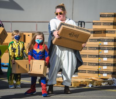 Dressed for the season, from left, Josephine Kulland, 4, as Marvel character Loki, Georgiana Gewock, 7, as Captain America and Rachael Gewock as a flying squirrel, participate in delivering food boxes to arriving vehicles Friday at 11016 E. Montgomery Drive in Spokane Valley.  (DAN PELLE/THE SPOKESMAN-REVIEW)