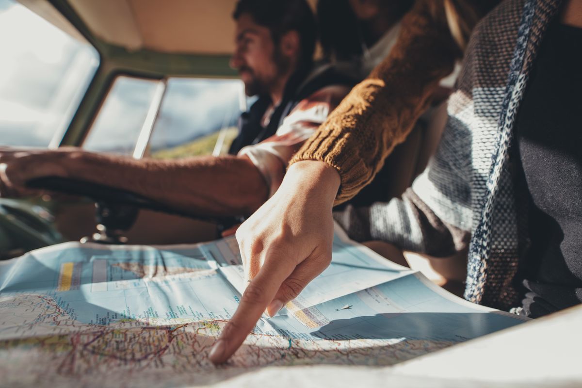 Friends on road trip looking at map for directions. Close up of female pointing at the map while man driving van in background.  (jacoblund)