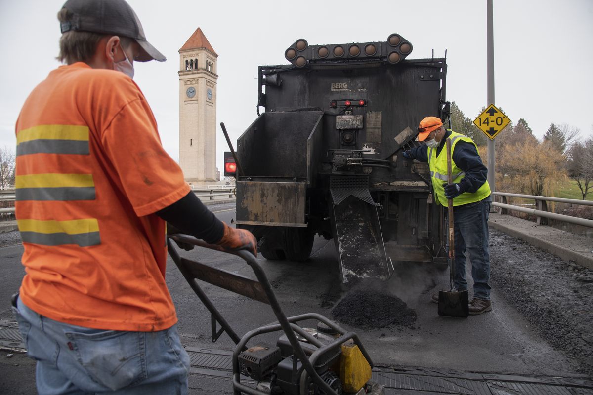 Street Department worker Kelly Stevens, left, holds a clattering machine that will pack the patching material into a pothole as Alex Mizner, right, deposits patching material on Washington Street, north of Spokane Falls Boulevard Friday, Jan. 21, 2022. Midwinter pothole repair requires heating up cold patch materials to help it adhere to the roadway.  (Jesse Tinsley/THE SPOKESMAN-REVIEW)