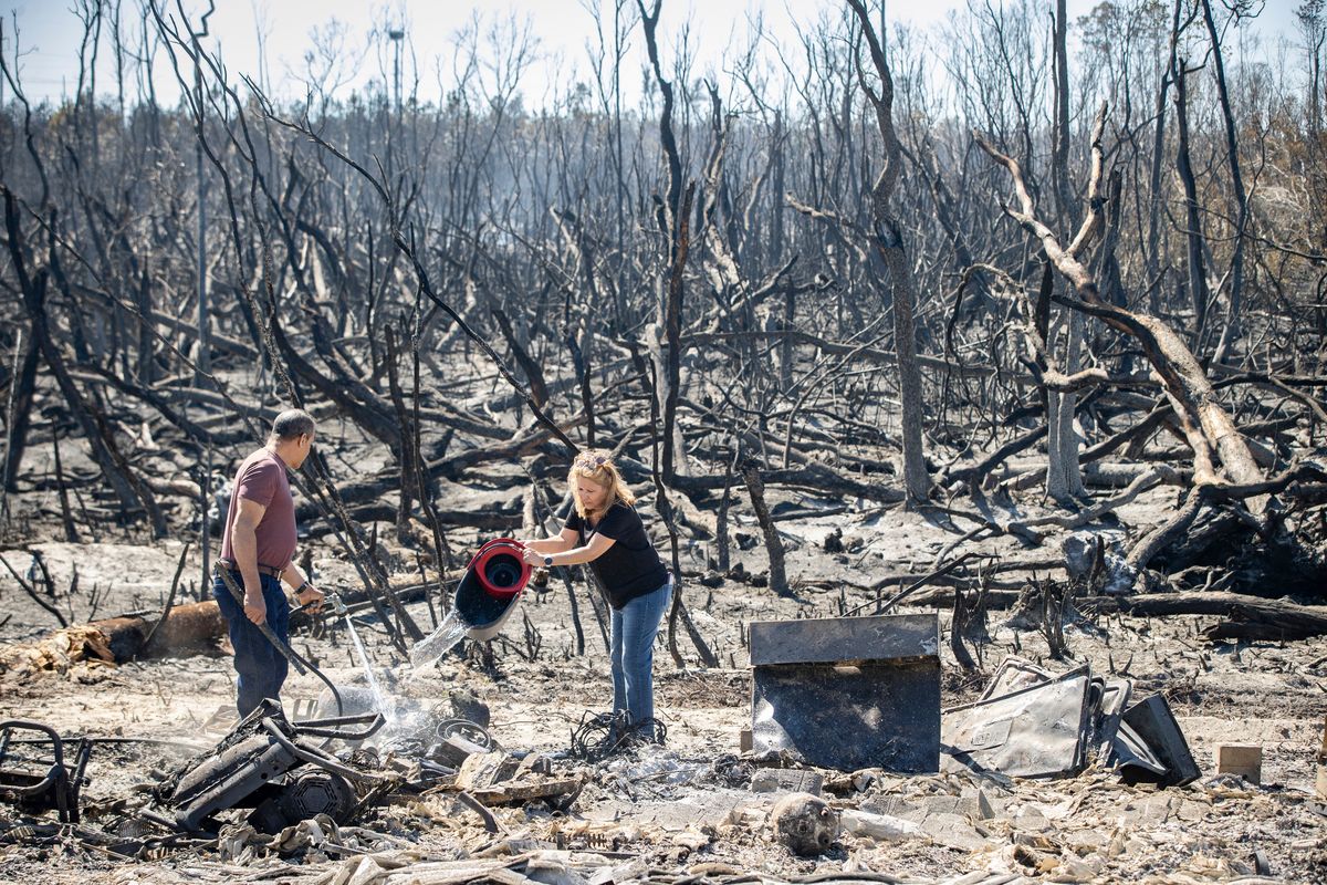 Hector Rivera and Wandi Blanco put water on hotspots behind their home in Panama City, Fla., Saturday, March 5, 2022, following a wildfire that started Friday. The fire destroyed two homes next to them and melted the siding off of their home.  (Mike Fender)