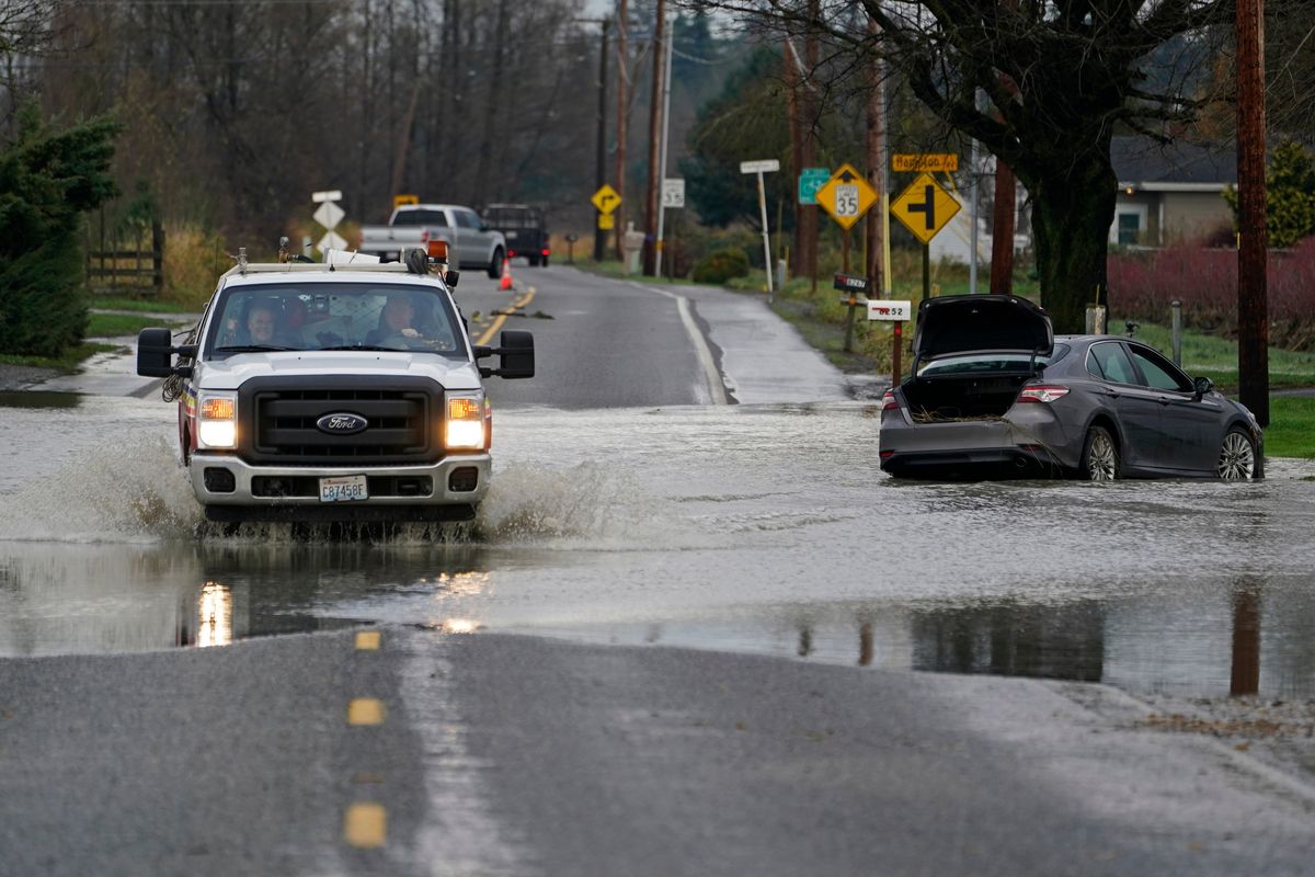 A truck drives through water over a road near Everson, Wash., Monday, Nov. 29, 2021 past a car that was stranded by flooding in the area earlier in the month. Localized flooding was expected Monday in Washington state from another in a series of rainstorms, but conditions do not appear to be as severe as when extreme weather hit the region earlier in November.  (Elaine Thompson)