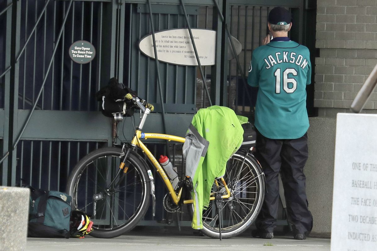 Al Jackson, a die-hard Seattle Mariners fan and season-ticket holder, takes a photo through the bars at the home-plate entrance of T-Mobile Park during last year’s pandemic-shortened season, when fans weren’t allowed into the ballpark.  (Associated Press)