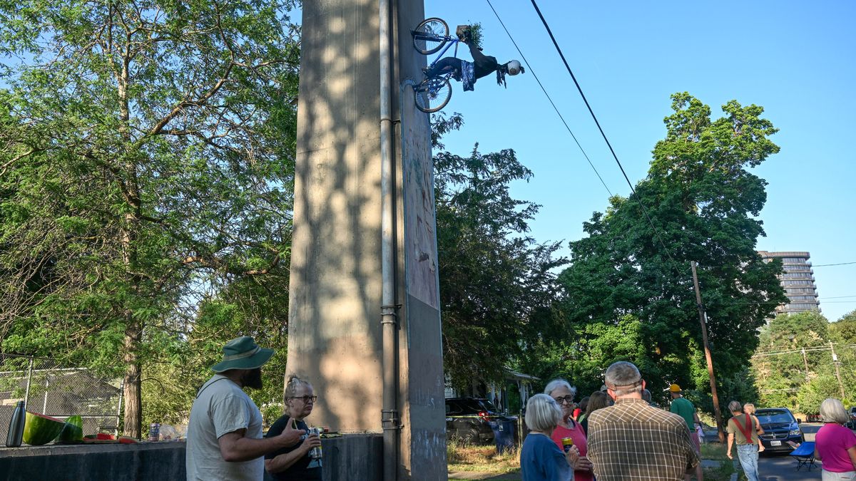 Neighbors gather in the Peaceful Valley neighborhood and look up at the sculpture of a bicyclist mounted to one of the Maple Street Bridge