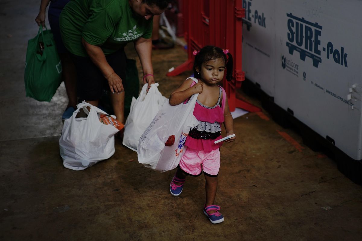 In this Sept. 13, 2018 photo, a girl helps her mother carry donated food and other staples handed out to needy residents by the MARC Ministry, a non-profit charity in Manati, Puerto Rico. Charity workers say the number of needy lining up for food has doubled since the storm, and there are days when they run out of food. (Ramon Espinosa / Associated Press)