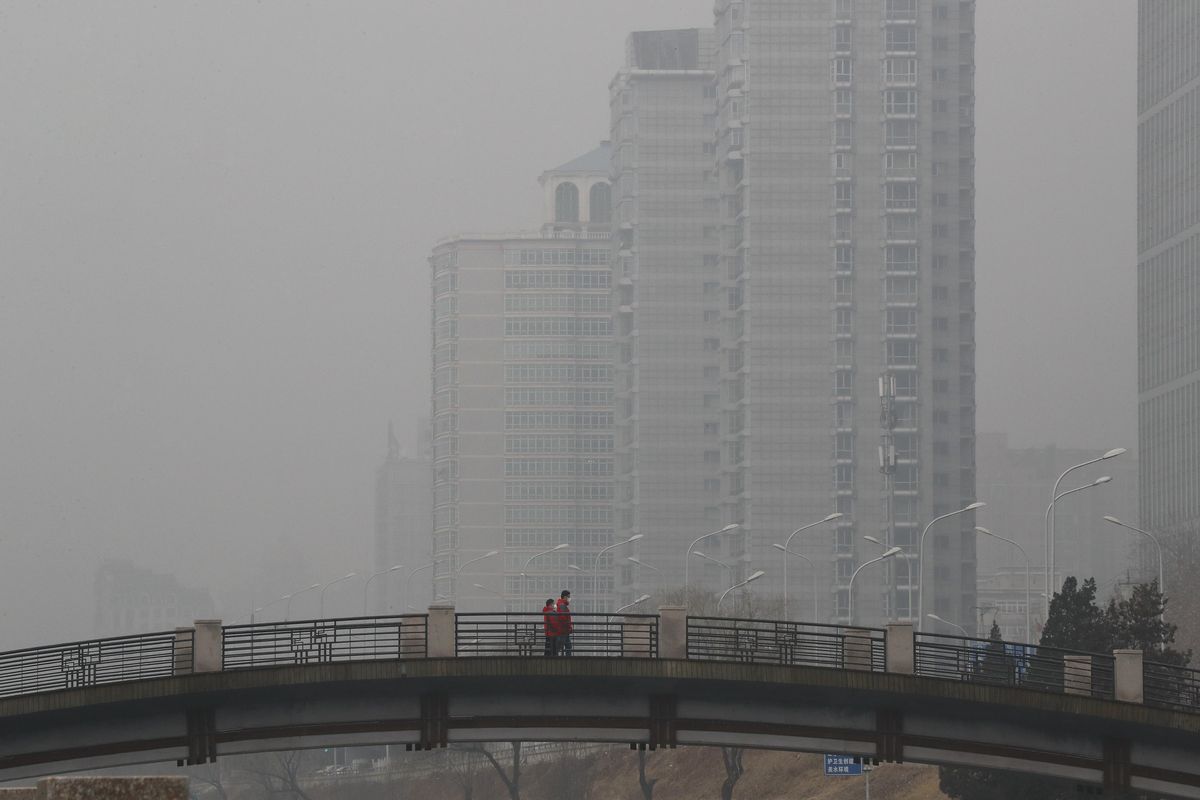 In this Jan. 5, 2017, file photo, Chinese men wearing masks to filter the pollution walk on a bridge near building shrouded by fog and pollution in Beijing. (Andy Wong / Associated Press)