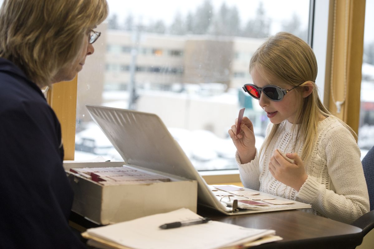 Grace Klinkenberg, 7, takes a test from vision therapist Chris Hill, left, that uses glasses with red and green filters to check for binocularity, the coordinated use of both eyes, on Jan. 29 at the office of Dr. Todd Wylie. (Jesse Tinsley)