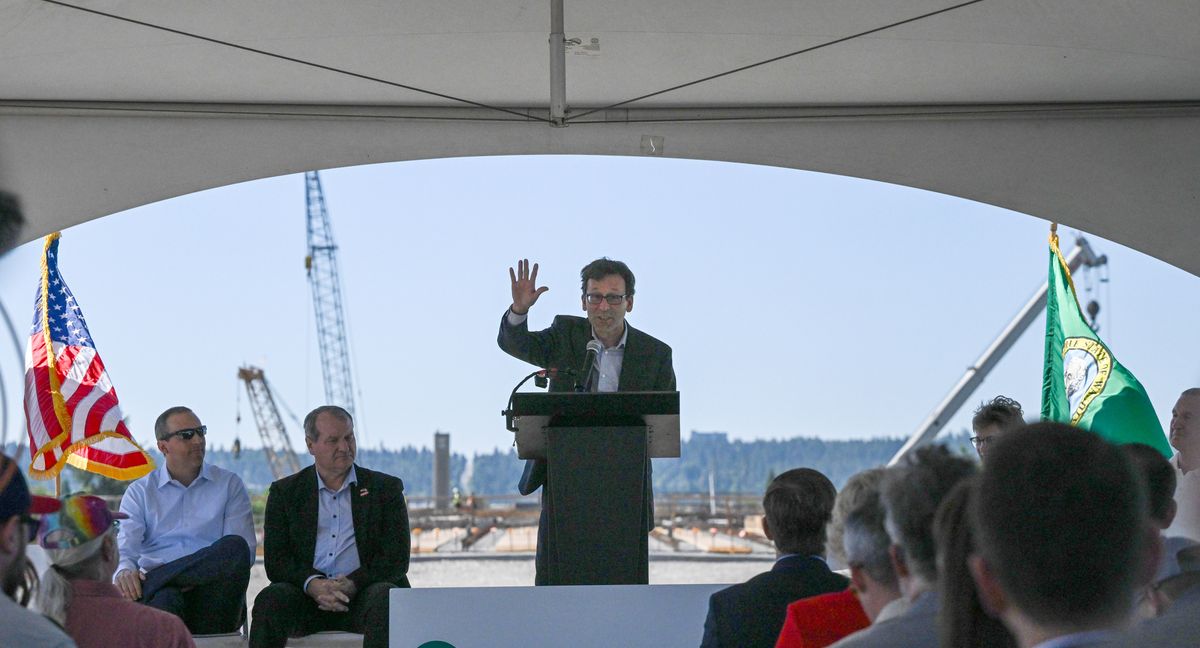 Under a tent with a backdrop of freeway construction, Gov. Bob Ferguson gives a news conference about the final push to complete the north-south corridor from the Spokane River and Spokane Community College area to I-90. The news conference was near the construction of the elevated deck of the freeway taking shape over the Spokane River. (Jesse Tinsley/The Spokesman-Review)