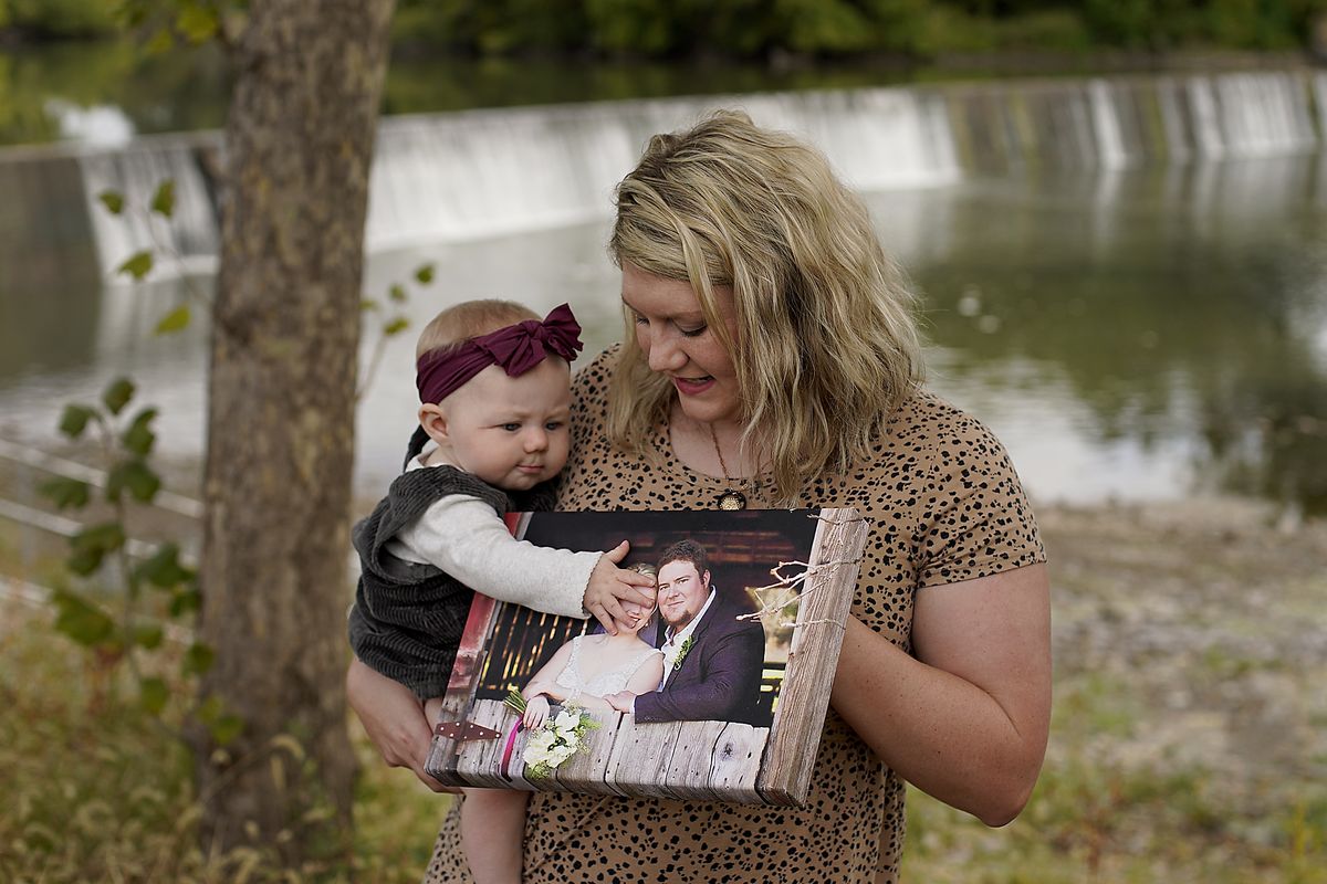 Aubrea Baker displays her wedding photo as she and her 7-month-old daughter Haylen visit one of her late husband