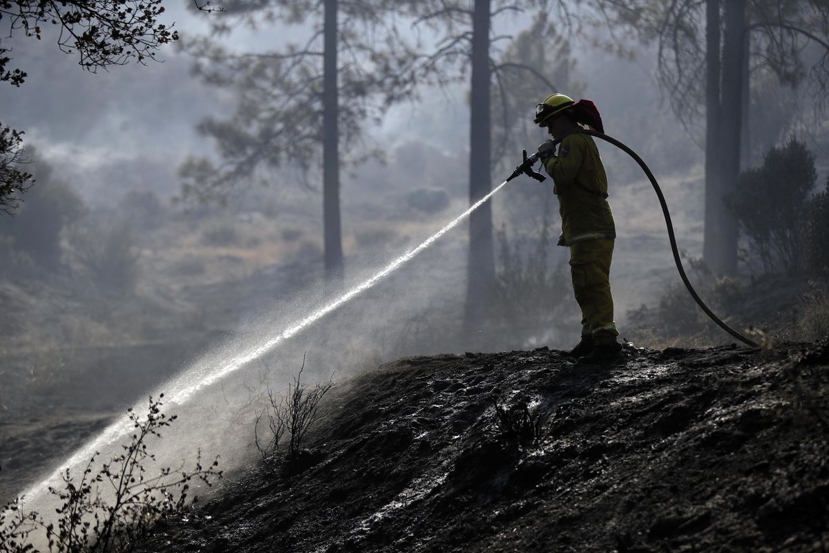A firefighter hoses down hot spots along Highway 243 on Thursday, July 26, 2018, near Idyllwild, Calif. A fast-moving wildfire tore through trees, burned several homes and forced evacuation orders for an entire mountain town as California sweltered under a heat wave and battled ferocious fires at both ends of the state. (Marcio Jose Sanchez / Associated Press)
