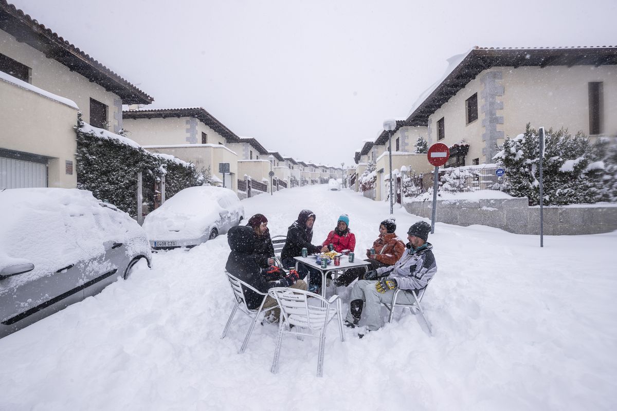 Neighbours have drinks in the middle of the street during a heavy snowfall in Bustarviejo, outskirts of Madrid, Spain, Saturday, Jan. 9, 2021. A persistent blizzard has blanketed large parts of Spain with 50-year record levels of snow, halting traffic and leaving thousands trapped in cars or in train stations and airports that suspended all services as the snow kept falling on Saturday. Half of Spain is on alert, with five provinces on their highest level of warning. (Bernat Armangue)