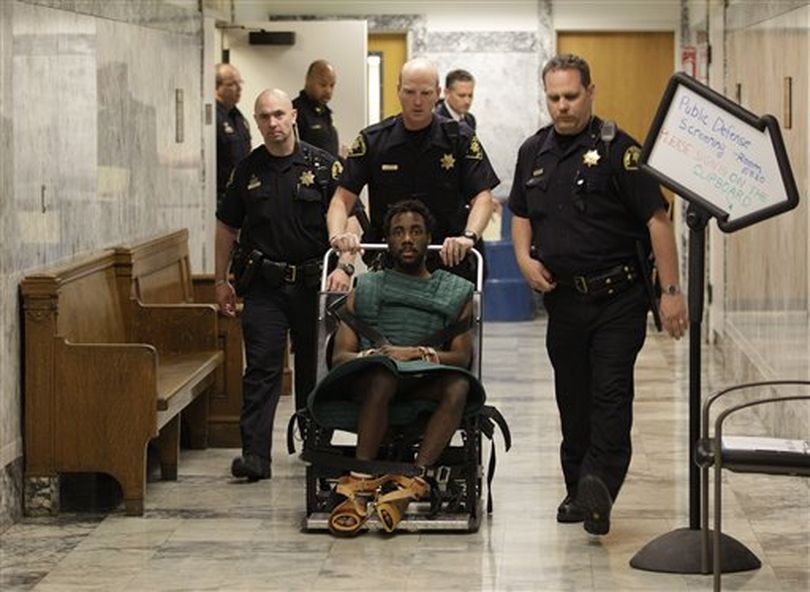In this May 12 photo, accused rapist and murderer Isaiah Kalebu, lower center, is taken in a wheeled restraint chair through a hallway at the King County Courthouse following a court hearing in Seattle. Judge Michael C. Hayden has taken the unusual step of tentatively barring Kalebu from attending his own trial when opening statements began in King County Superior Court on Monday because of outbursts during pre-trial hearings. Instead, Kalebu will be able to watch the proceedings via closed-circuit television from a nearby courtroom.  ((AP Photo/Ted S. Warren))