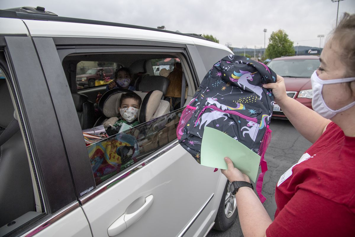 At the annual Salvation Army backpack giveaway, volunteer Shelby Coates, right, holds up a unicorn-themed backpack which doesn’t thrill three-year-old Matthew Jordan, left, but pleases his sister, five-year-old Adelina Jordan sitting in the far back seat of the car in the parking lot of the Spokane Fair and Expo Center, Wednesday, Aug. 12, 2020. Each backpack contained school supplies appropriate for the age of the child. The Salvation Army, with a large donation from Cenex stores, gave out thousands of backpacks in drive-through fashion Wednesday. Dozens of volunteers helped distribute the backpacks.  (Jesse Tinsley/The Spokesman-Review)