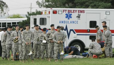 Members of the 1st Infantry Division band stand at rest while medics work on a tuba player who was hit by a sky diver during ceremonies at Fort Riley, Kan., Thursday.  (Associated Press / The Spokesman-Review)