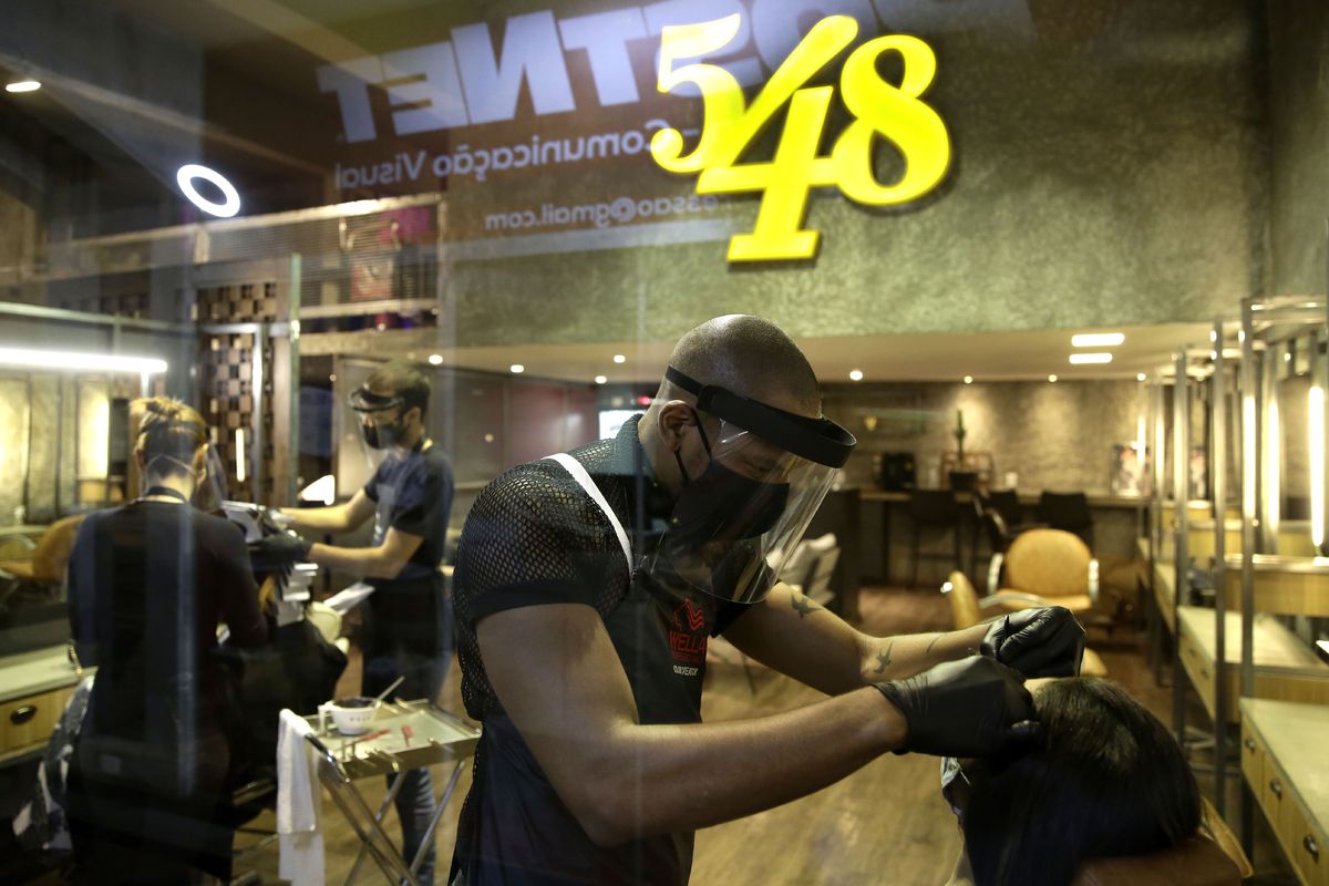 A hairdresser wears a face shield, mask, and gloves for protection amid the COVID-19 pandemic while attending a client on the first day the saloon was allowed to reopen, as restrictions ease in Brasilia, Brazil, Wednesday, July 15, 2020.  (Eraldo Peres)