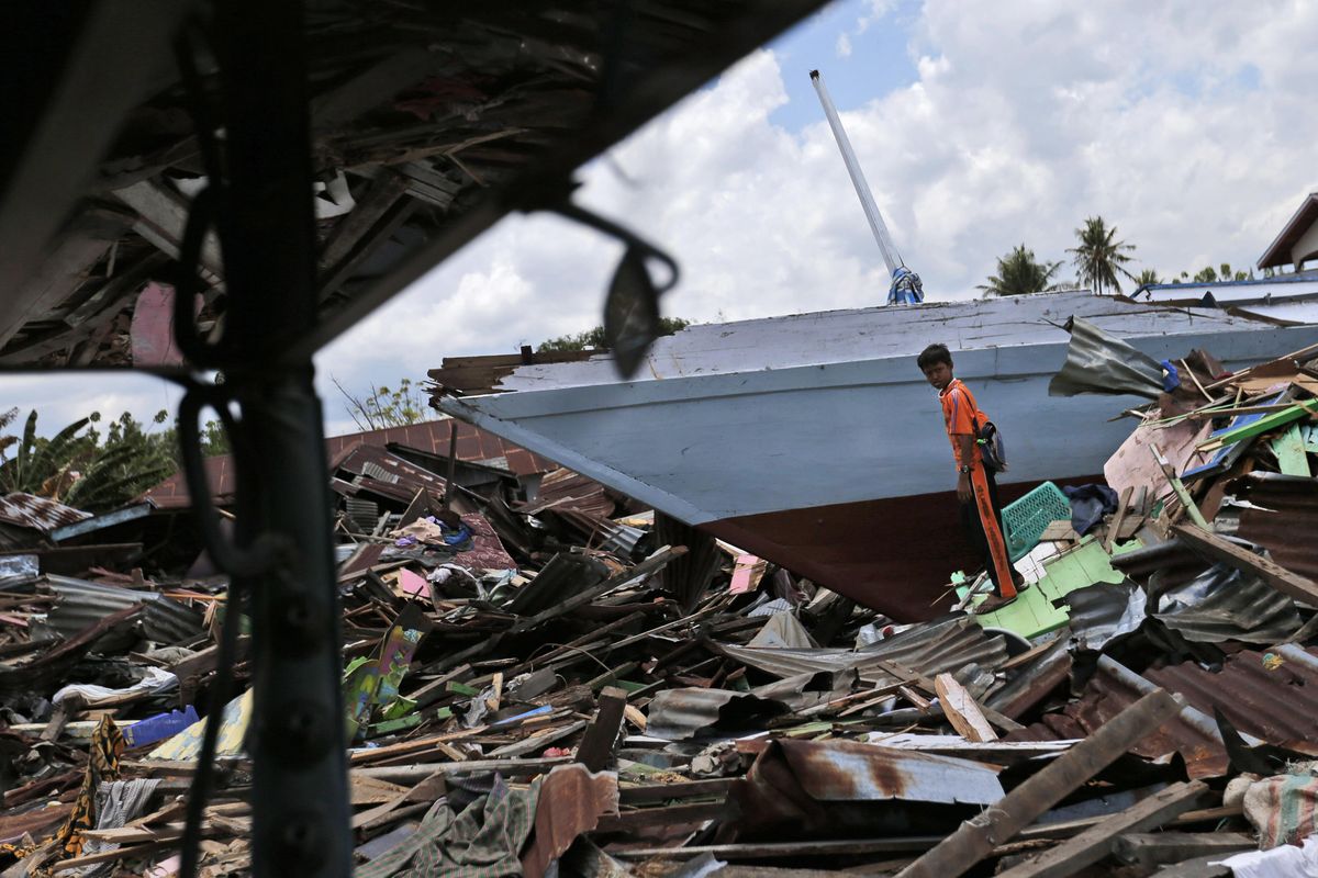 A young man stands near a boat swept ashore by the tsunami in Wani village on the outskirt of Palu, Central Sulawesi, Indonesia, on Wednesday, Oct. 10, 2018. (Dita Alangkara / AP)