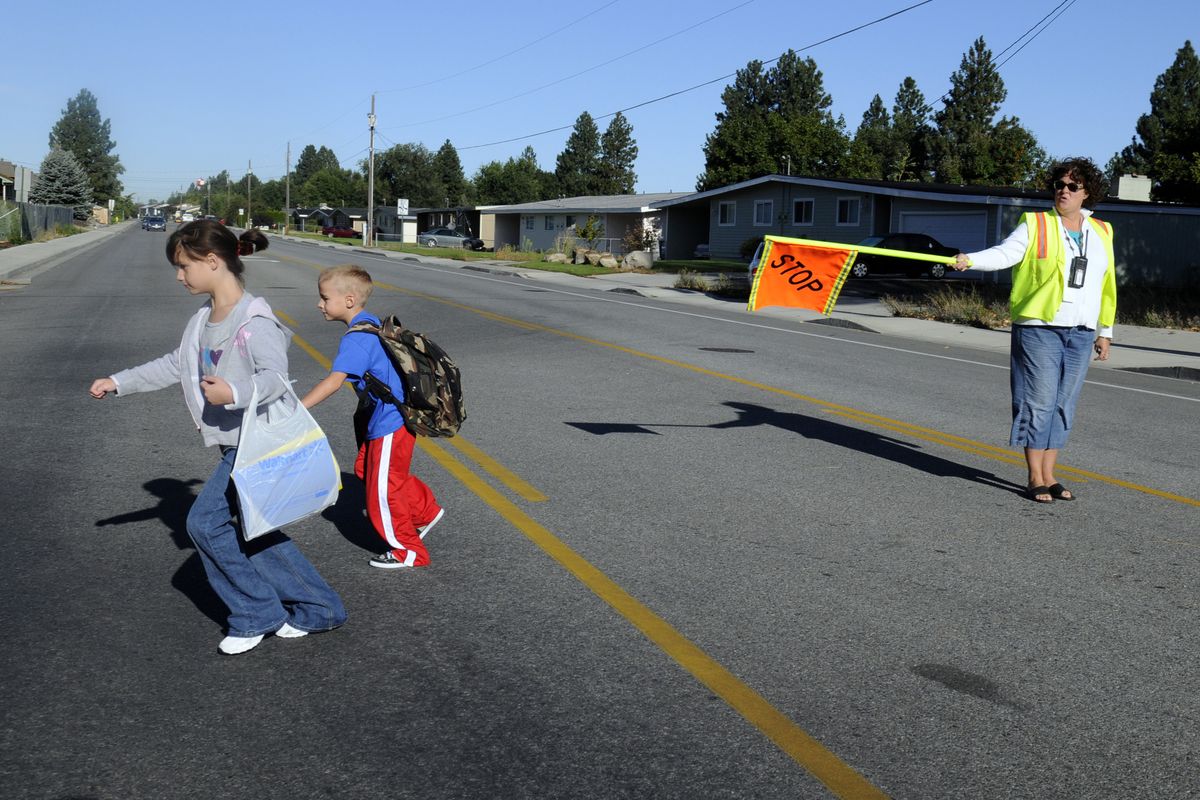 Progress Elementary crossing guard Vicky Seward directs third-grader Ty James and her brother, second-grader Koter James, across Mission Avenue  on the first day of school Tuesday. Their bus route has been eliminated because of budget cuts, so Seward leads a “walking school bus” to escort a group of kids to school every day. (J. BART RAYNIAK / The Spokesman-Review)